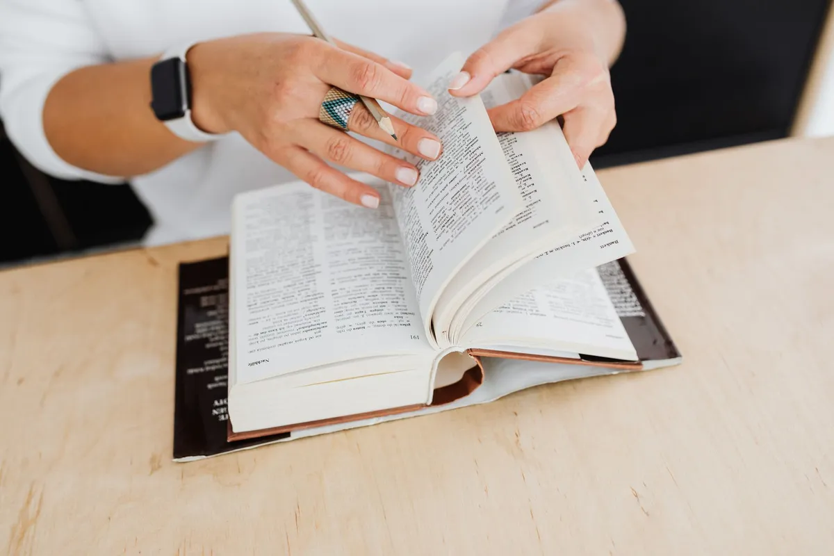 Hands turning the pages of a dictionary on a desk