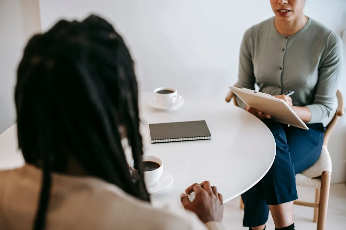 A woman with a clipboard talking to a client across a table with coffee