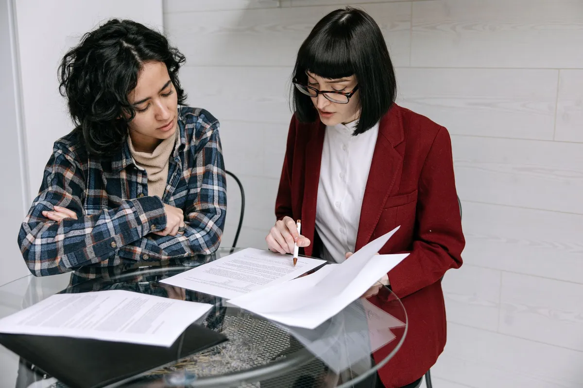 Two people at a table going through printed pages together, one sitting with folded arms