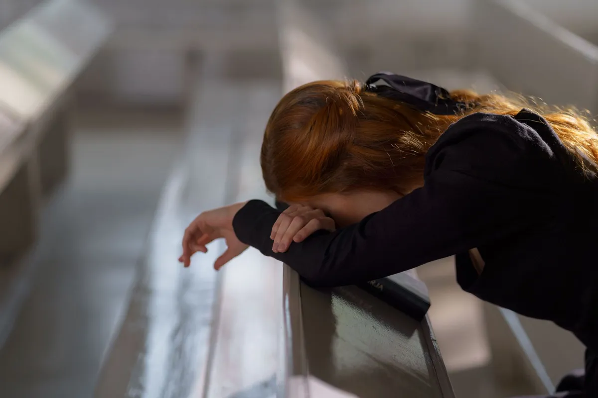 A woman leaning forward onto a church pew with her head on her arms