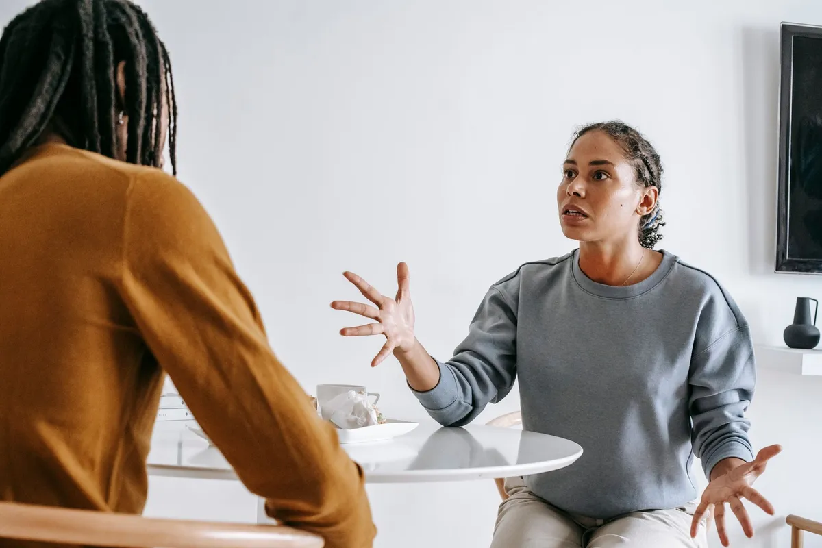 A woman talking with her hands raised to a man sitting across a small table