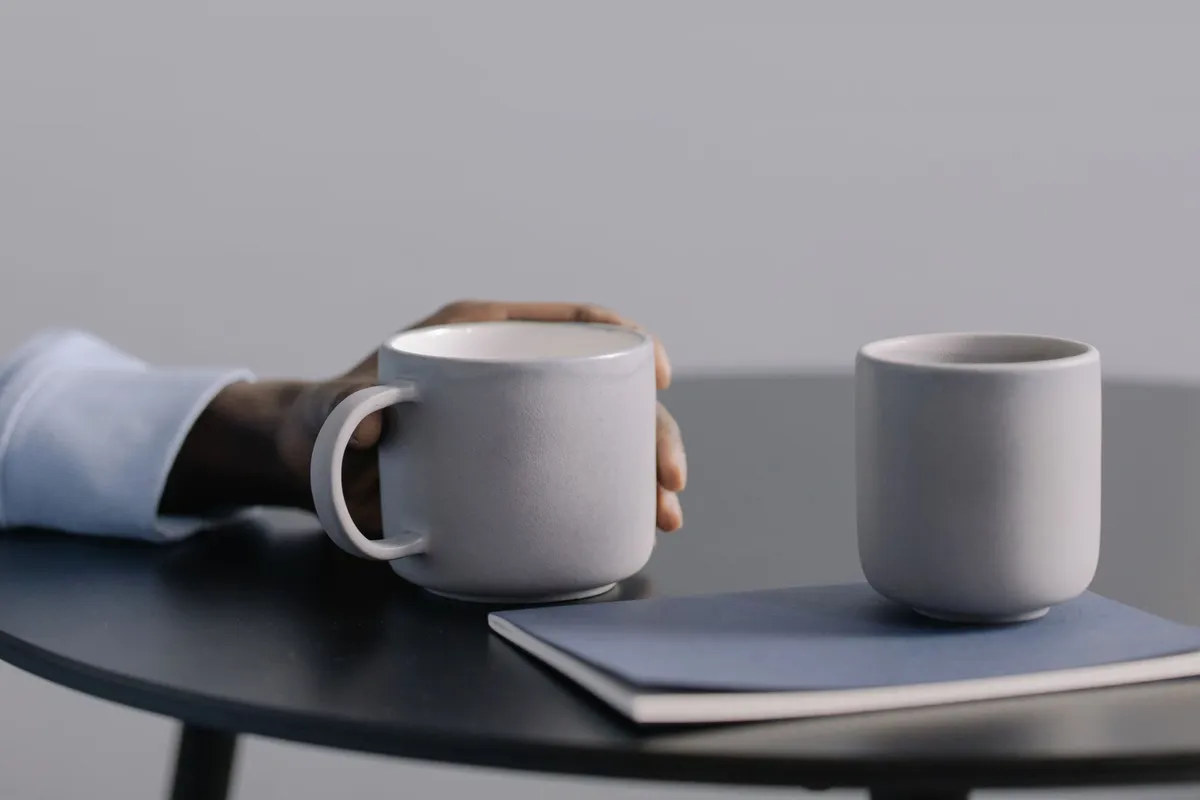 Two coffee mugs held across a kitchen table