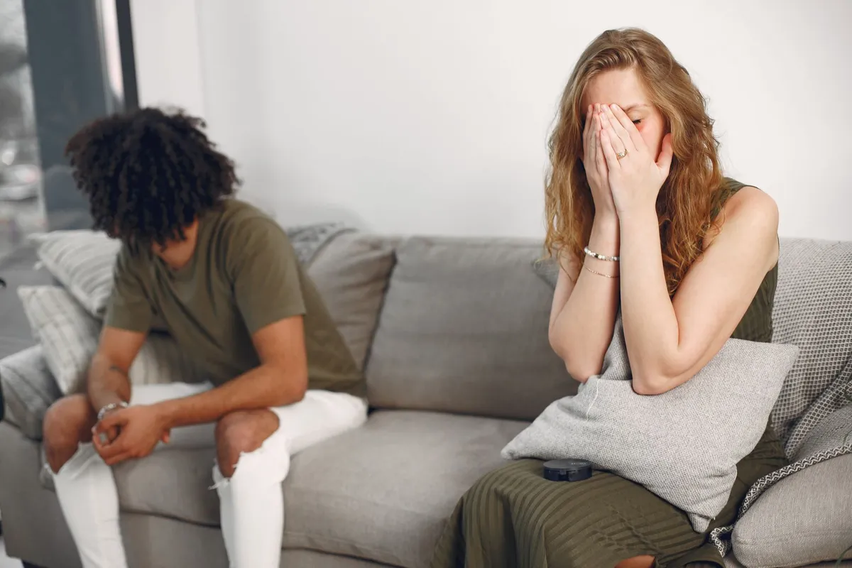 A couple sitting apart on a sofa with visible emotional distance between them