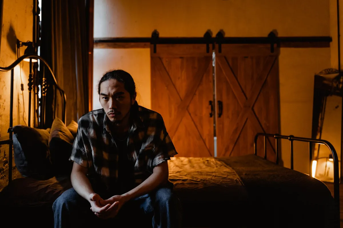 A man sitting alone on the edge of a bed at night, thinking my wife hates me