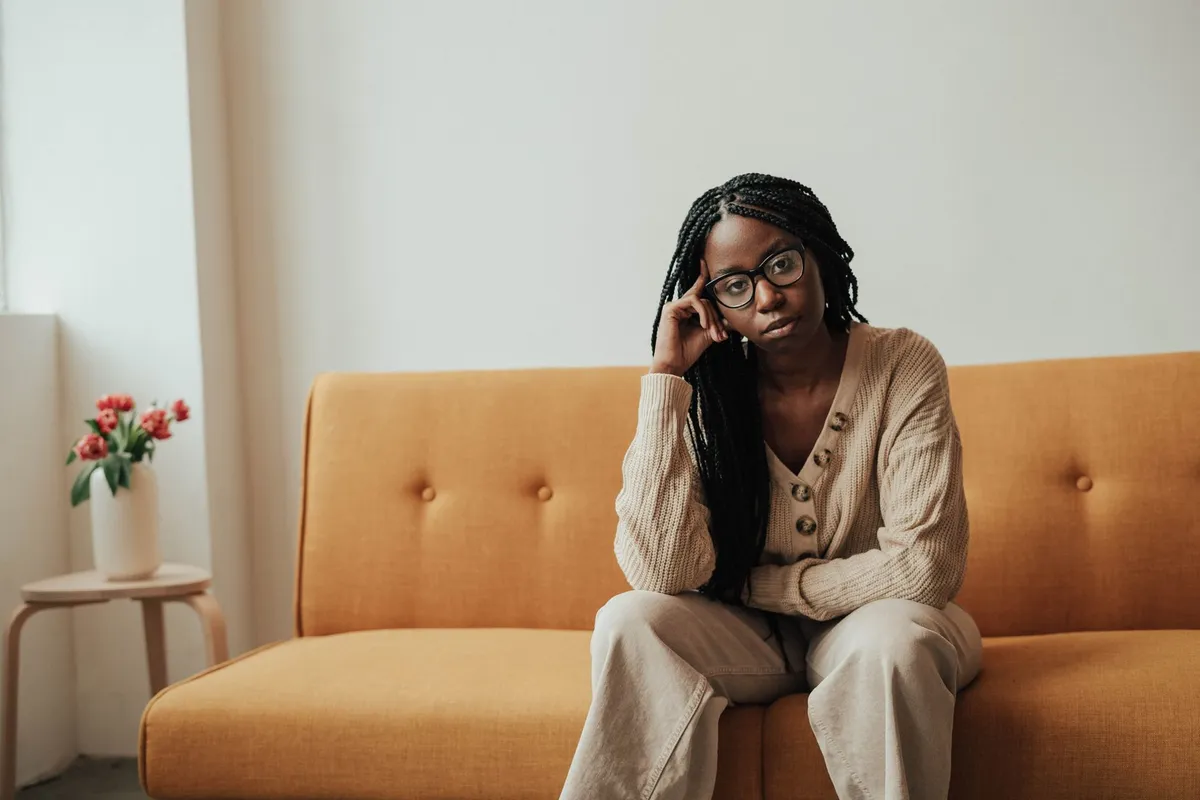 A woman sitting alone on a sofa in daylight resting her head against her hand