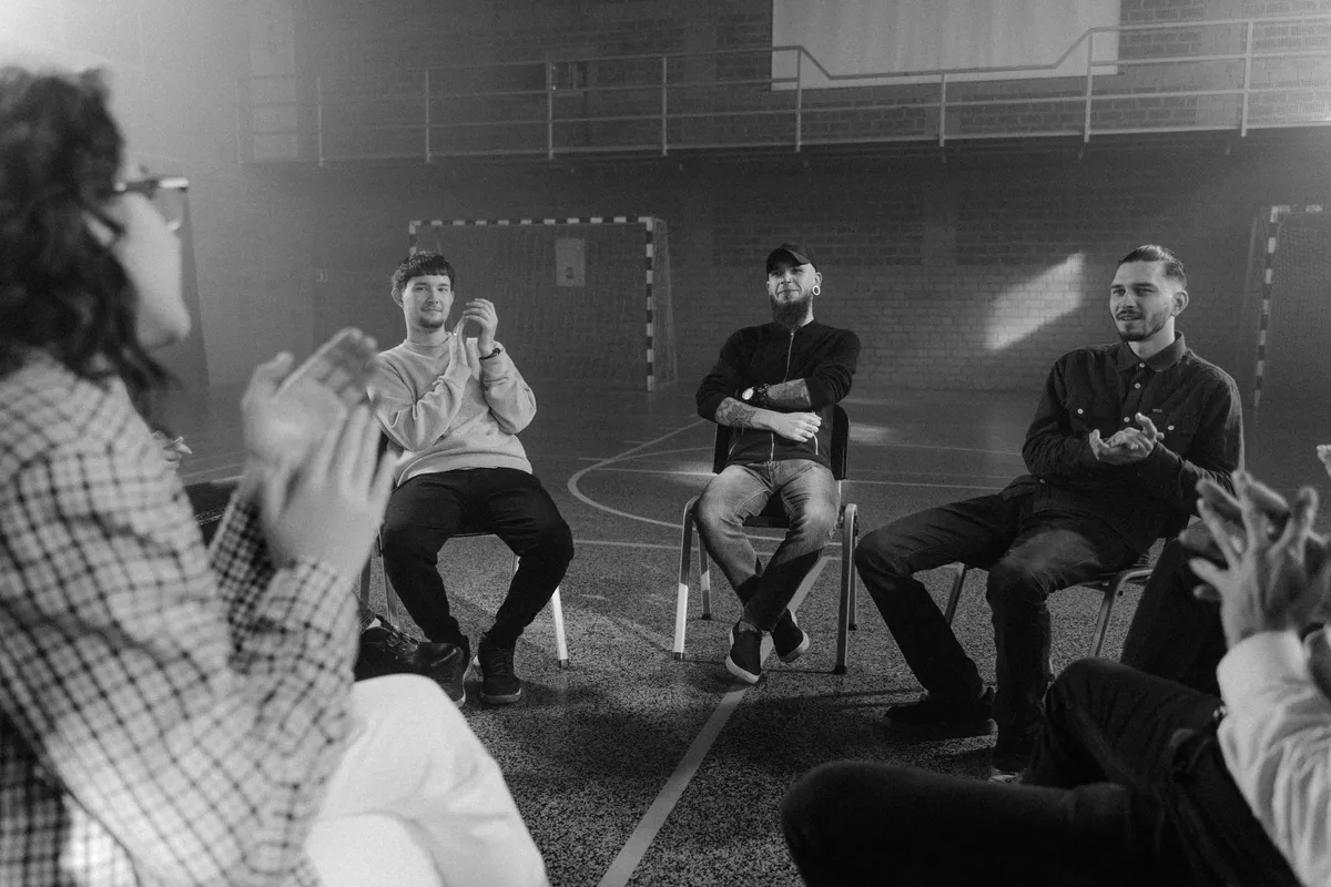 A group of men sitting in a circle talking, the group work that supports individual therapy