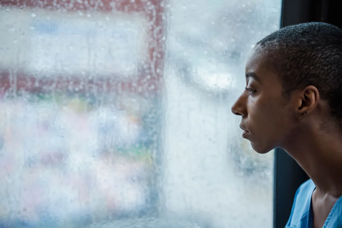 A person looking out of a rain-covered window, caught in the cycle of a trauma bond