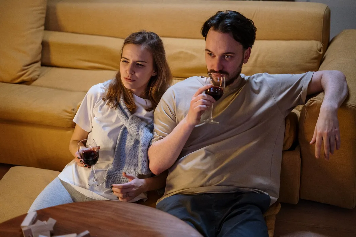 A couple sitting at opposite ends of a sofa in the evening, the quiet distance of a silent divorce
