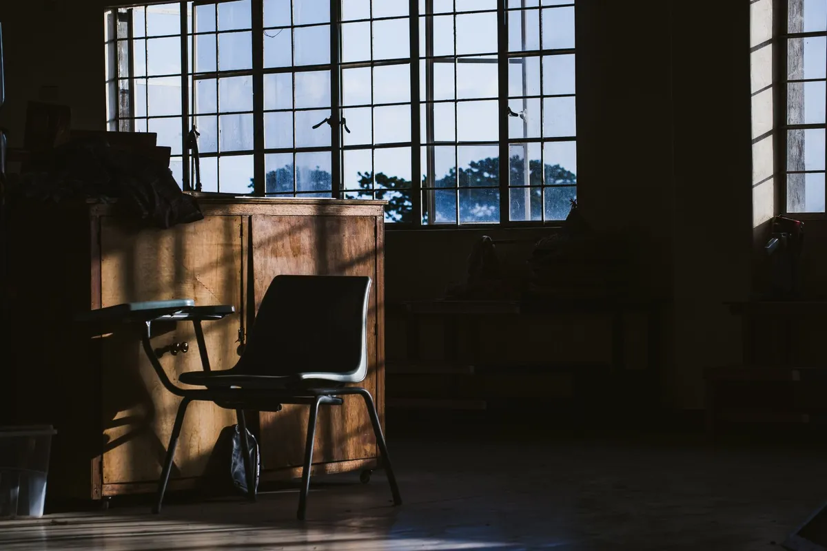 An empty chair by a window in a quiet room, the stillness of a marriage nobody is reaching across