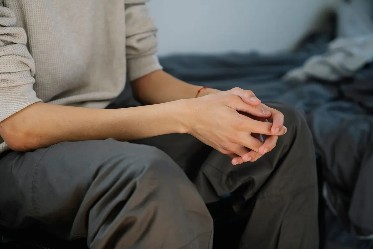 A man sitting on the edge of a bed with his hands clasped