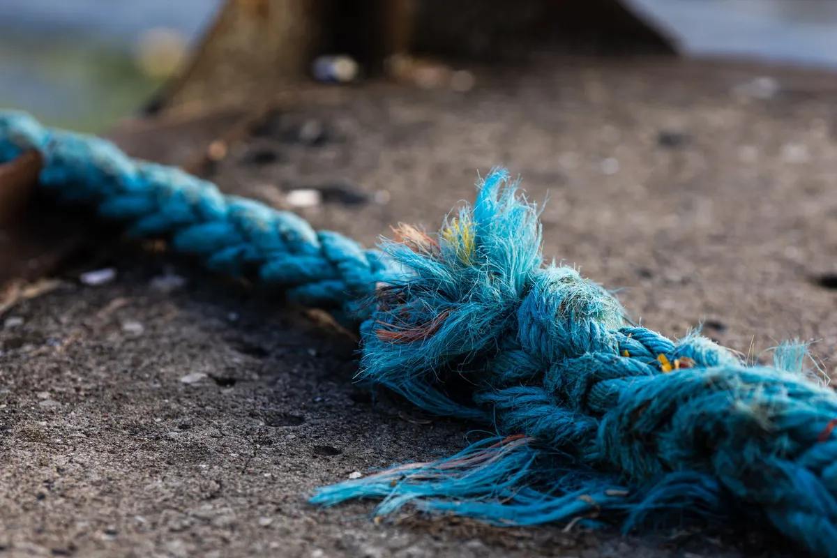 A close-up of a frayed and knotted blue rope lying on concrete
