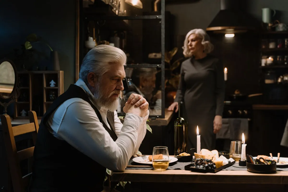 A couple sitting in silence at a table, the quiet distance an emotional affair grows in
