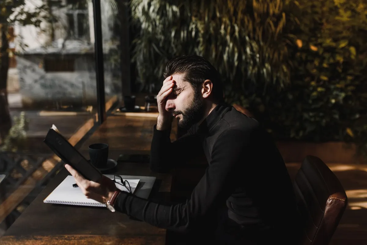 A man sitting at a table with his hand pressed to his forehead