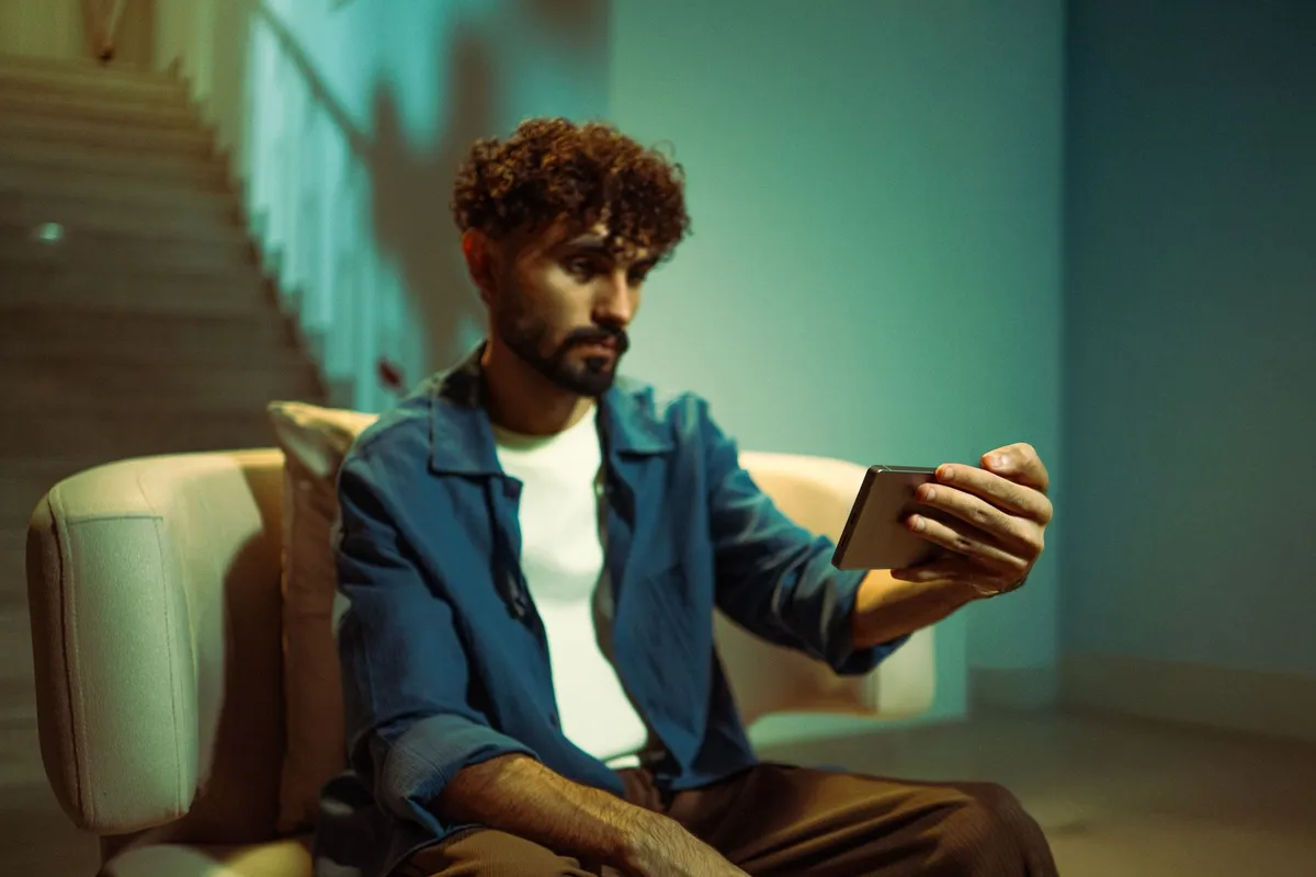 A man sitting on a sofa at home looking at his phone in the evening